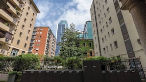 A multi-story residential building with balconies, a central tree, and a modern glass building in the background. - Garibaldi's Residence (Milan)
