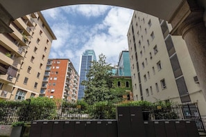 Ein mehrgeschossiges Wohngebäude mit Balkonen, ein Baum in der Mitte und ein modernes Glasgebäude im Hintergrund.