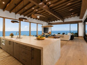 Een moderne keuken met een groot eiland, houten balken in het plafond en uitzicht op zee.