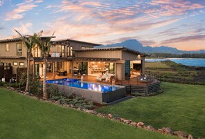 Ein modernes, zweistöckiges Haus mit Pool, Sitzgelegenheiten im Freien und Blick auf den Ozean und die Berge.