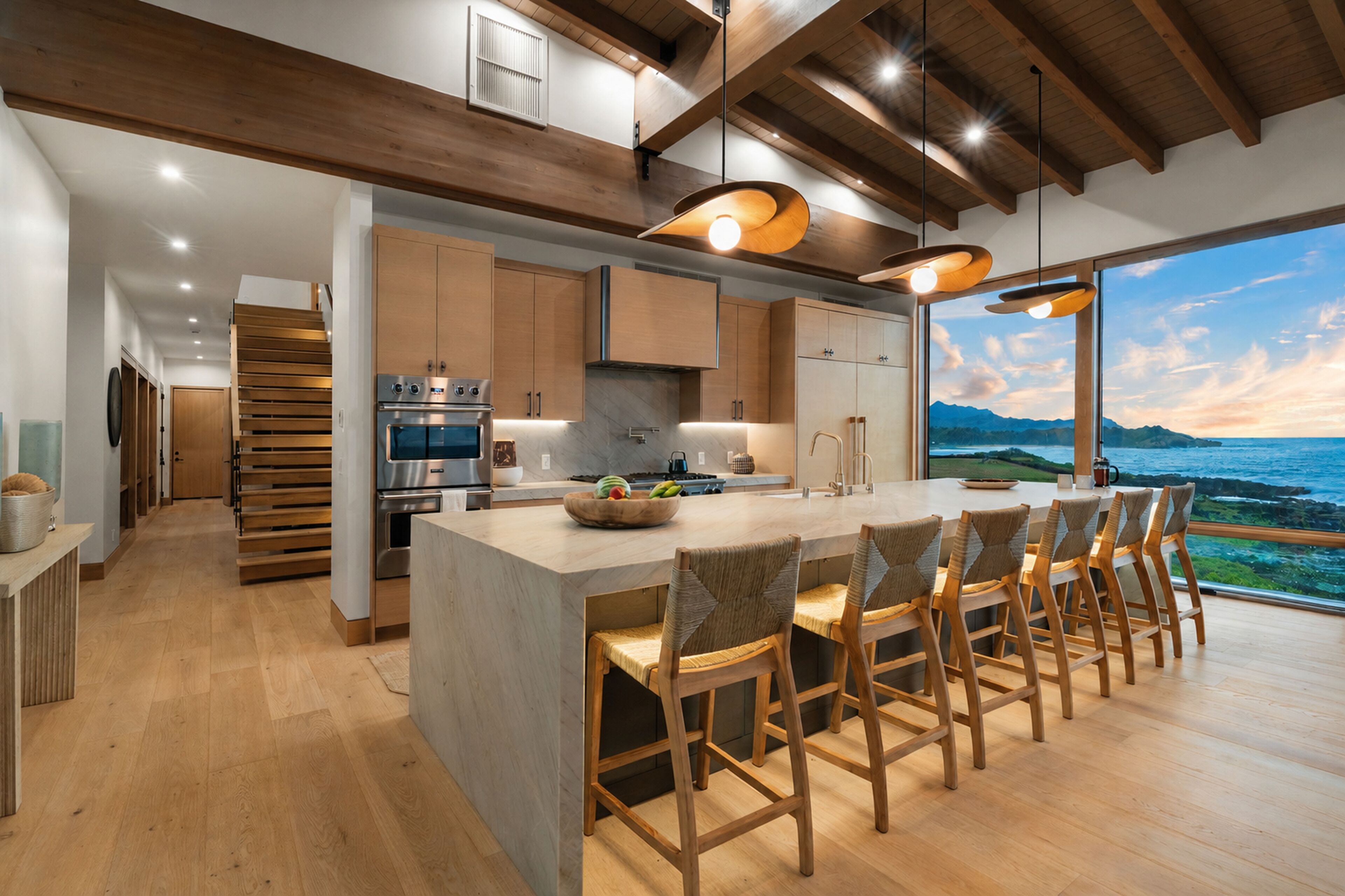 A modern kitchen with a large island, wooden bar stools, and a view of the ocean.