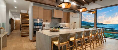A modern kitchen with a large island, wooden bar stools, and a view of the ocean.