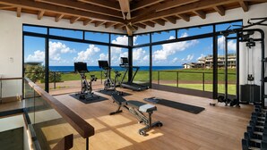 Ett gym med träningsutrustning, stora fönster och utsikt över havet.