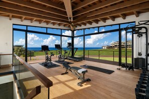 Ein Fitnessstudio mit Trainingsgeräten, großen Fenstern und Meerblick.