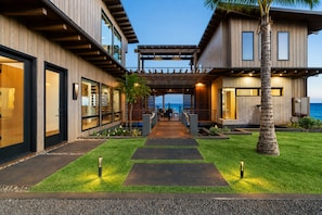 Een modern huis met twee verdiepingen, een overdekt terras, een verzorgd gazon en uitzicht op de oceaan.