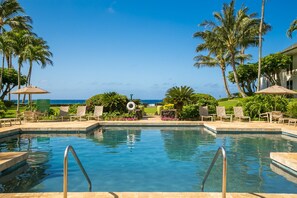 Ein Pool mit klarem, blauem Wasser, umgeben von Liegestühlen und Palmen, mit Blick auf den Ozean im Hintergrund.
