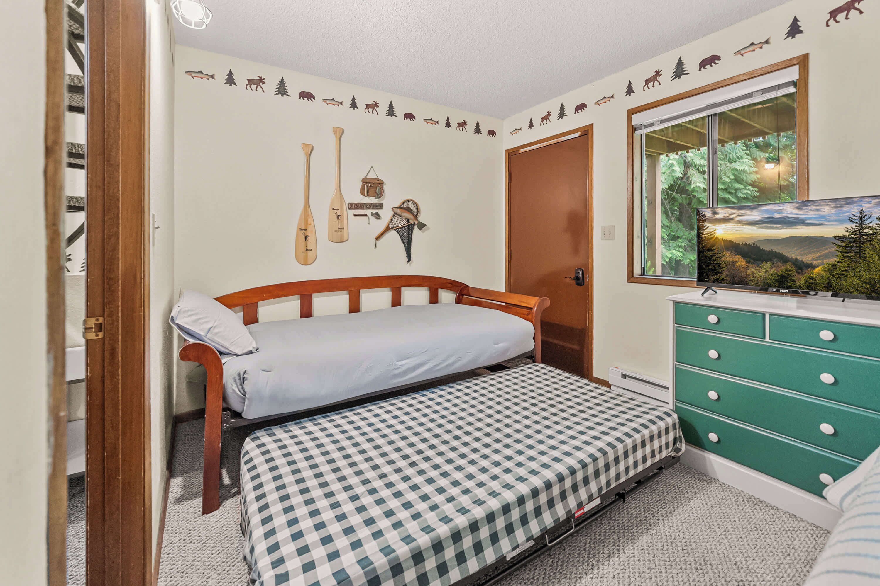 A bedroom with a bed, a dresser, a wall decal, and a window with a view.