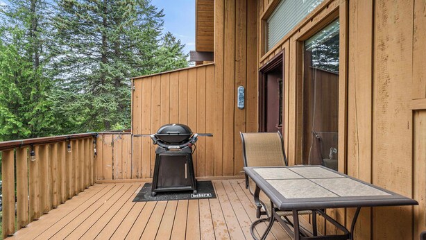 Een houten terras met een barbecue, een tafel en een stoel.