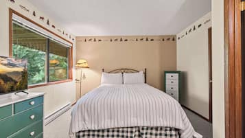 Een slaapkamer met een bed, een dressoir, een lamp en een raam.