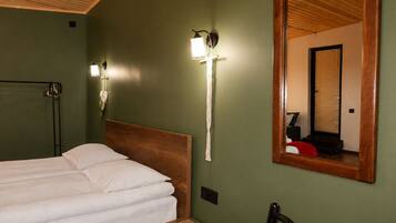 Habitación con una cama, cabecera de madera, lámpara de pared y un espejo que refleja una ventana con persianas.