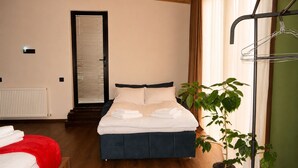 Ein ordentlich bezogenes Bett mit weißen Leinen, einer roten Decke und einer Blumentopf-Pflanze daneben.