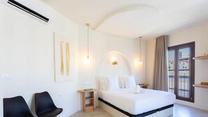 A modern hotel room with a large bed, two black chairs, a small wooden nightstand, and a view of the city through the window. - Deluxe Quadruple Apartment (Alicante)