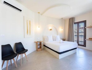 A modern hotel room with a large bed, two black chairs, a small wooden nightstand, and a view of the city through the window. - Deluxe Quadruple Apartment (Alicante)