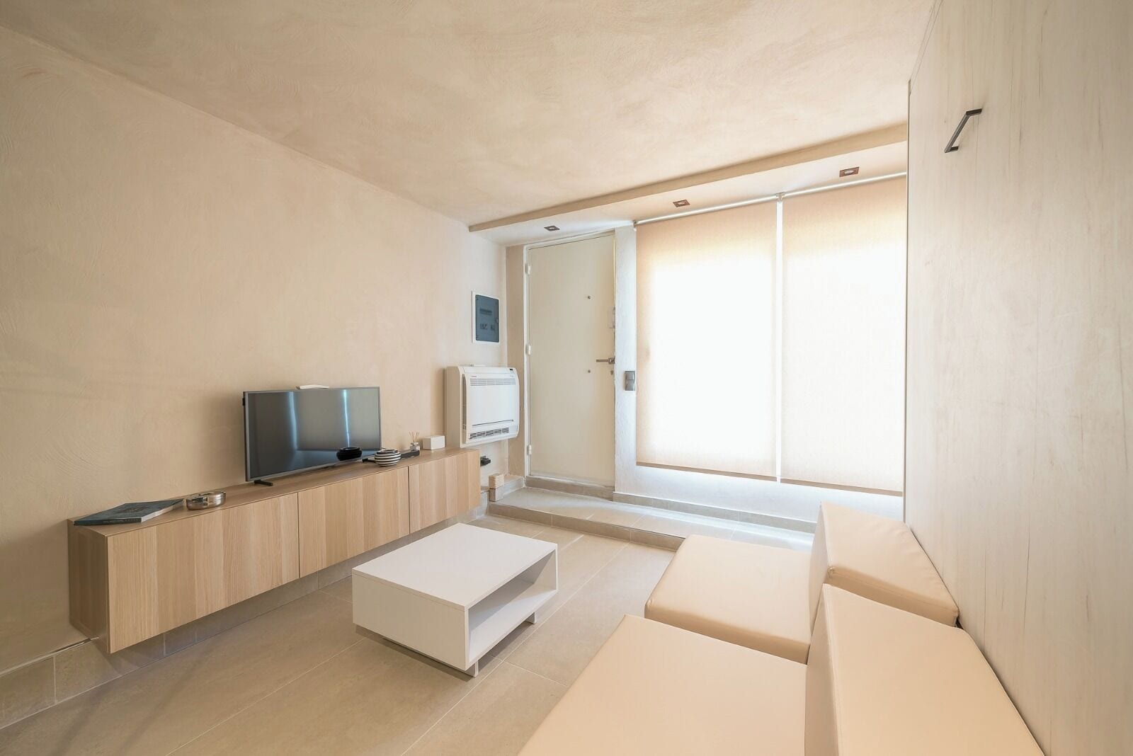 A modern living room with a flat-screen TV, a white coffee table, and a sliding door leading to a balcony.