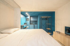 A bedroom with a bed, a small table, and a TV. There is a kitchenette in the background with a sink and cabinets. - Brand New Modern Studio in Faliro - 
Private garden (Paleo Faliro)