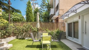 A patio with artificial grass, a table, chairs, and a covered umbrella. - Brand New Modern Studio in Faliro - 
Private garden (Paleo Faliro)