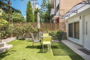 Eine Terrasse mit Kunstgrasanlage, einem Tisch, Stühlen und einem überdachten Sonnenschirm.