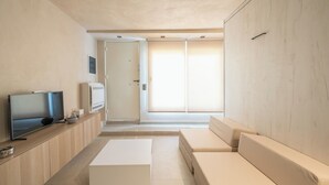 A modern living room with a flat-screen TV, a white sofa, a coffee table, and a sliding door leading to a balcony. - Brand New Modern Studio in Faliro - 
Private garden (Paleo Faliro)