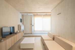 Ein modernes Wohnzimmer mit Flachbildfernseher, einem weißen Sofa, einem Couchtisch und einer Schiebetür, die auf einen Balkon führt.