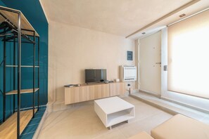 A modern, minimalist room with a flat-screen TV, a white console table, a built-in air conditioning unit, and a large sliding door. - Brand New Modern Studio in Faliro - 
Private garden (Paleo Faliro)