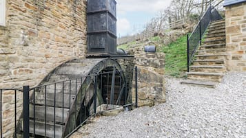 Un edificio de piedra con una rueda hidráulica y una escalera.