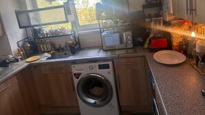 A compact kitchen with a washing machine, a microwave, and a sink. - Cozy London Apartment With View (London)