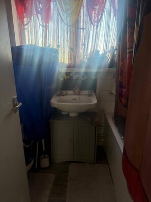 Ein kleines Badezimmer mit Waschbecken, Spiegel und einem Fenster mit Vorhängen.