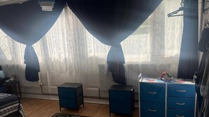 A bedroom with a bed, a desk with drawers, a radiator, and a window with curtains. - Cozy London Apartment With View (London)