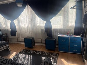 Ein Schlafzimmer mit Bett, Schreibtisch mit Schubladen, Heizkörper und einem fenster mit Vorhängen.