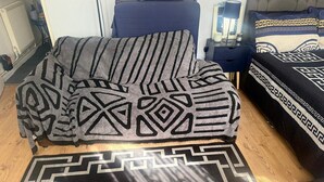 A room with a bed, a chair, a bedside table, and a rug with a geometric pattern. - Cozy London Apartment With View (London)