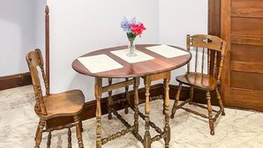 Et rundt spisebord i træ med fire stole, en vase med blomster, og en trædør i baggrunden.