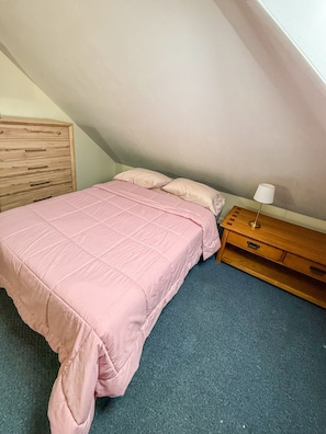 A single bed with a pink bedspread in a room with a sloped ceiling.