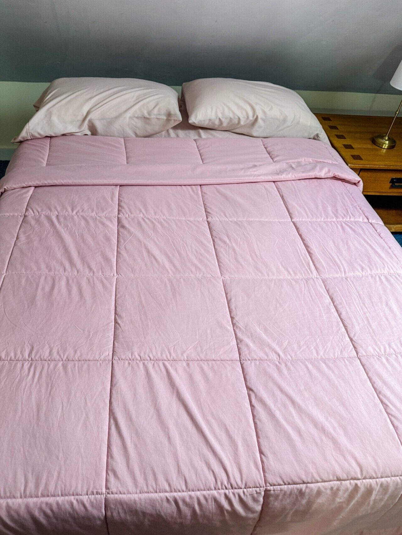 A bed with a pink quilt and two pillows.