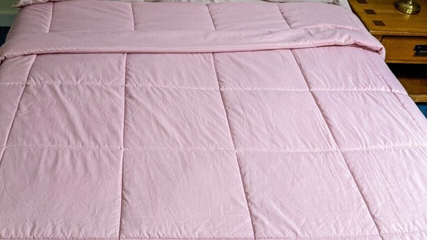 En seng med et pink sengetæppe og to puder.