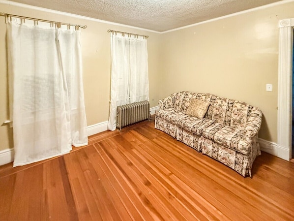 A room with wooden flooring, a radiator, and a floral-patterned sofa.