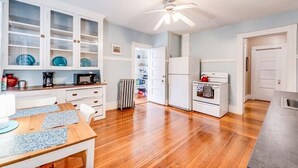 Une cuisine avec un plancher en bois, des armoires blanches, un ventilateur de plafond et un coin repas comprenant une table et des chaises.