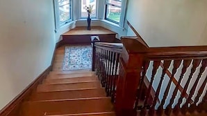 Un escalier en bois, doté d’une rampe, mène à un palier avec trois fenêtres.