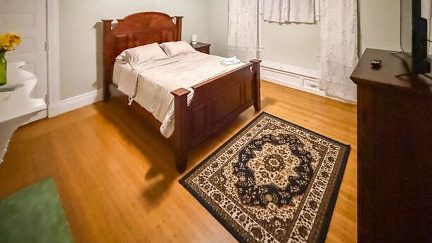 Une chambre à coucher avec un lit en bois, un tapis vert, une commode et une fenêtre avec des rideaux.