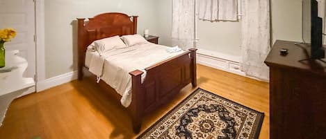Un dormitorio con una cama de madera, un tapete verde, un aparador y una ventana con cortinas.
