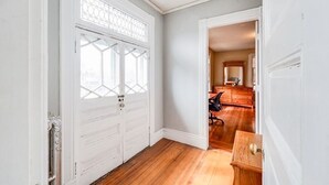 Un couloir avec une porte blanche donnant sur une pièce dont le sol est en bois et qui contient une commode.
