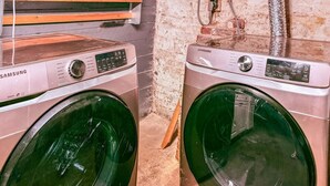 Deux machines à laver Samsung dans un espace buanderie, avec un mur en briques et une étagère en bois.