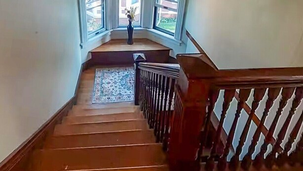 Un escalier en bois, doté d’une rampe, mène à un palier avec trois fenêtres.