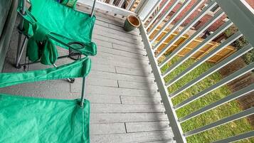 A balcony with a white railing, a green chair, and a small table.