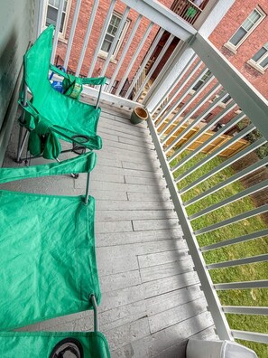 A balcony with a white railing, a green chair, and a small table.