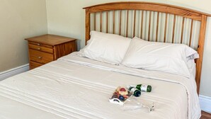Un lit bien fait, avec une tête de lit en bois, une petite table de chevet en bois et, sur le lit, un sac en plastique contenant des en-cas et une bouteille.