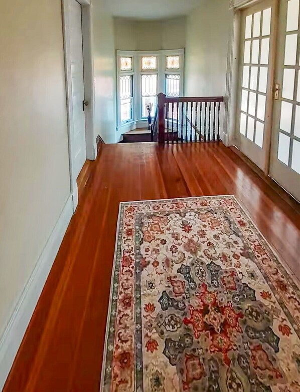 A hallway with wooden flooring, a patterned rug, and a staircase leading to an upper level.