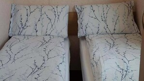 Dos camas individuales con estampado de ramas de árbol en la ropa de cama, en una habitación con paredes lisas.