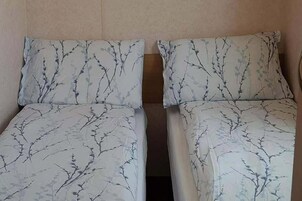 Dos camas individuales con estampado de ramas de árbol en la ropa de cama, en una habitación con paredes lisas.