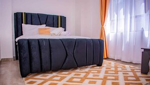 Una cama con cabecera negra, ropa de cama blanca y una alfombra estampada.