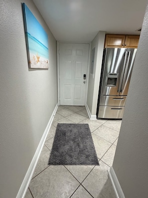 A hallway with a white door, a gray rug, and a stainless steel refrigerator. - Safe & Sound (Biloxi)